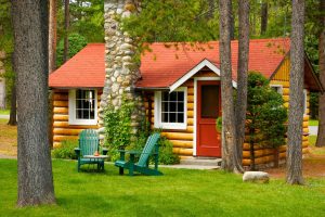 Heritage one room cabin exterior at Alpine village jasper. 2 Green chairs outside.