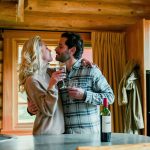 A romantic couple holding glasses of wine in their alpine village cabin