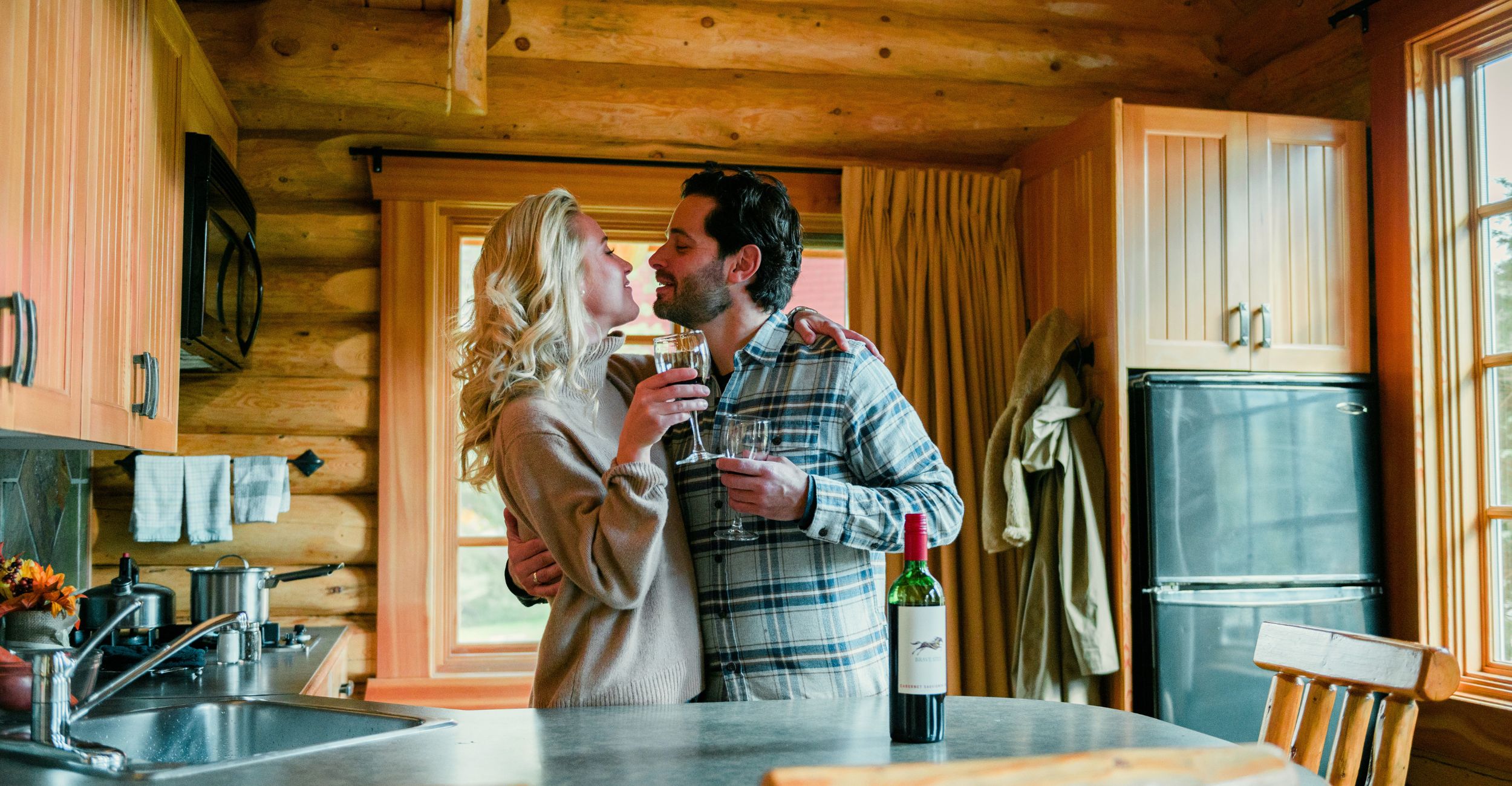 A romantic couple holding glasses of wine in their alpine village cabin